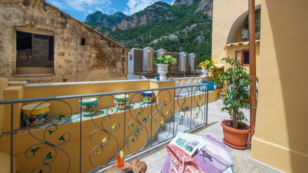 Ein Balkon mit Blick auf Berge, einem Blumentopf und einem Tisch mit einem Blumenstrauß.