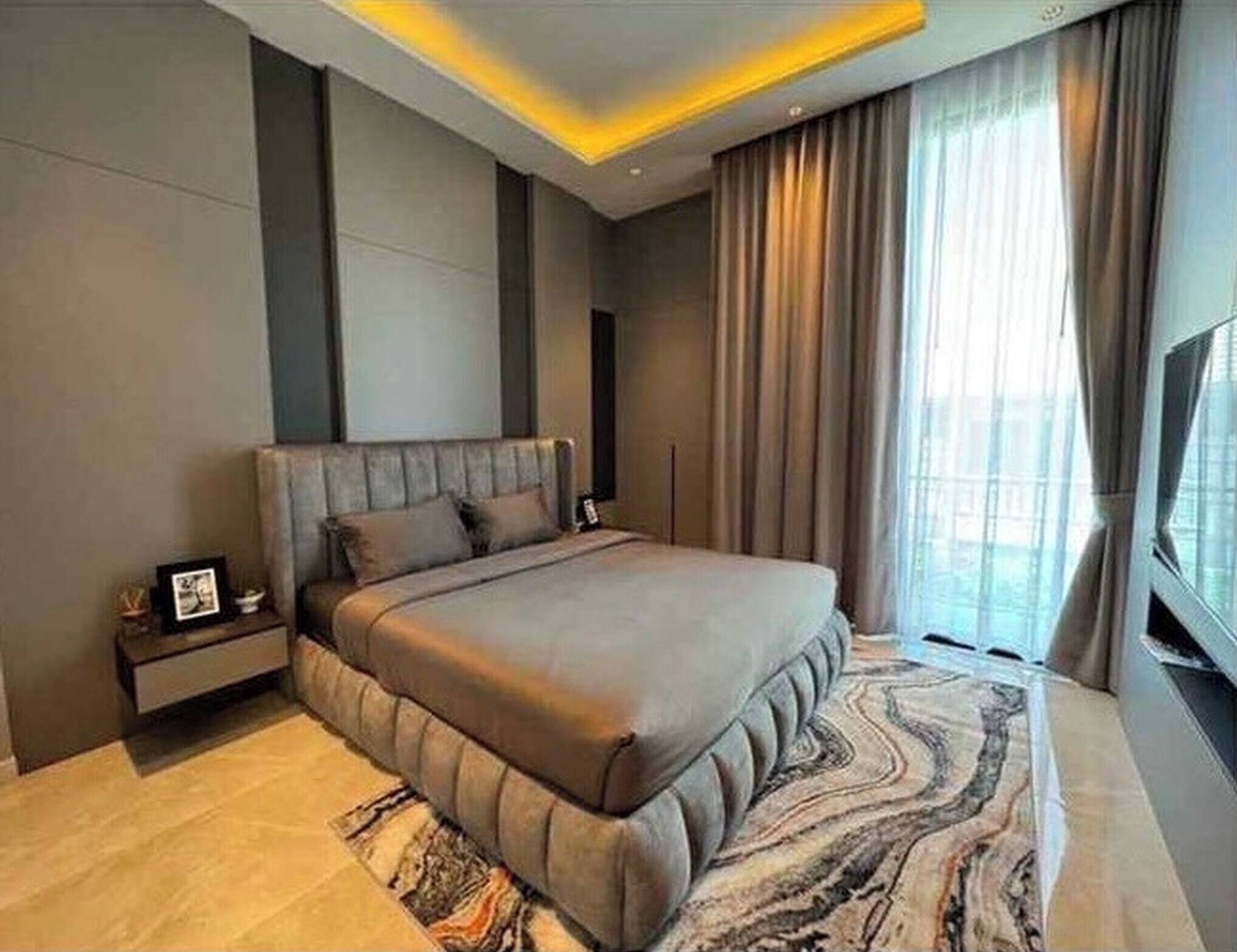 Un dormitorio moderno con una cama grande, una mesita de noche, un televisor y una ventana con cortinas.