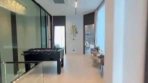 A modern interior with a foosball table, a glass partition, and a seating area with a table and chairs. - 5-bed Luxury Villa Pool&jacuzzi 5 Min to Walkingst (Pattaya)