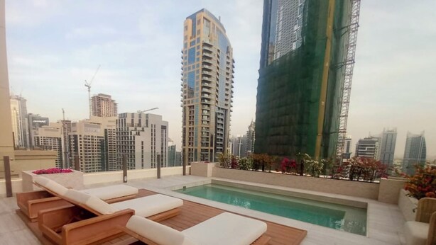 A rooftop pool area with lounge chairs and a view of surrounding high-rise buildings. - Maison Privee - Ultimate Luxury Penthouse w/ Pool & Marina Views (Dubai)