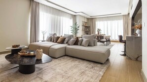 A modern living room with a sectional sofa, a round coffee table, and a dining area in the background. - Maison Privee - Ultimate Luxury Penthouse w/ Pool & Marina Views (Dubai)