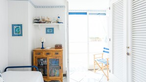 Ein Zimmer mit einem Bett, einem hölzernen Schrank voller Bücher, einem kleinen Tisch mit einer Lampe und einer Tür zu einem Außenbereich mit einem Stuhl.