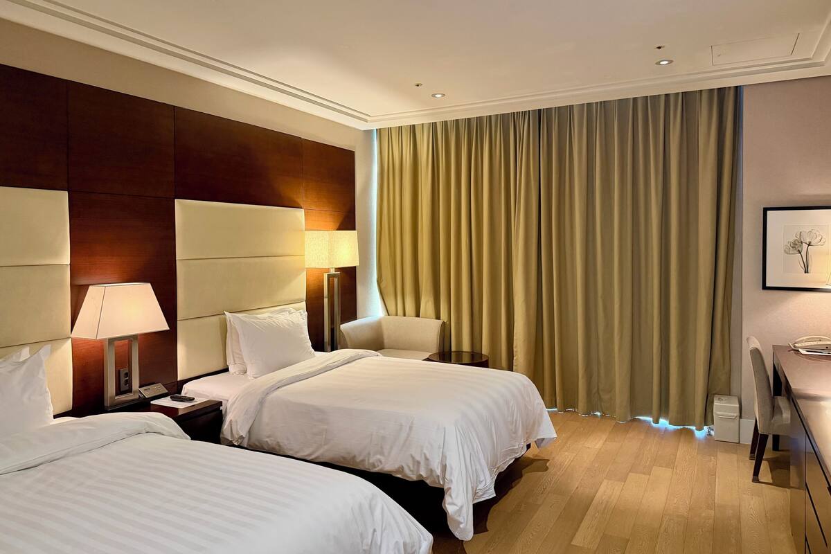 A hotel room with two beds, a desk, a chair, a lamp, and a curtain.
