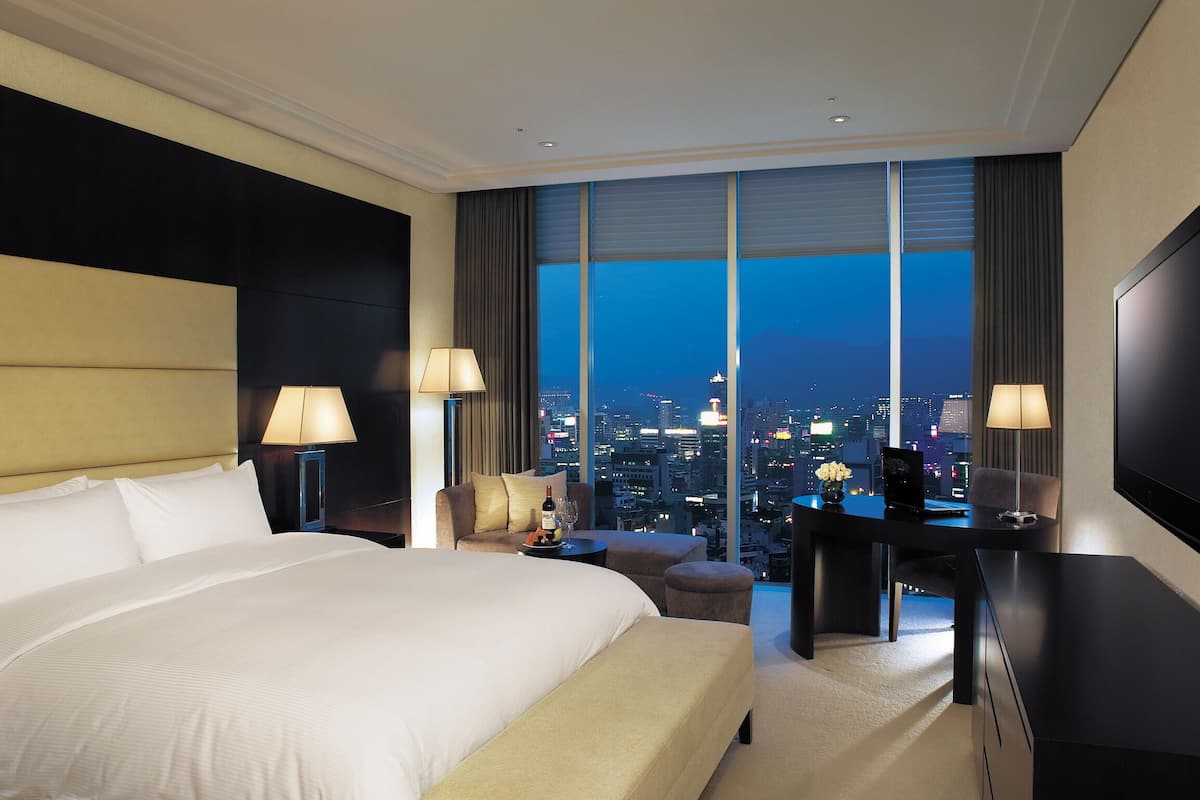 A hotel room with a large bed, a desk, and a view of the city at night.
