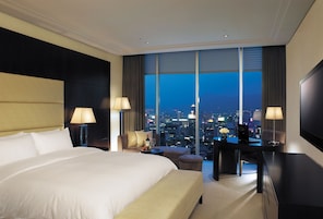 A hotel room with a large bed, a desk, and a view of the city at night.
