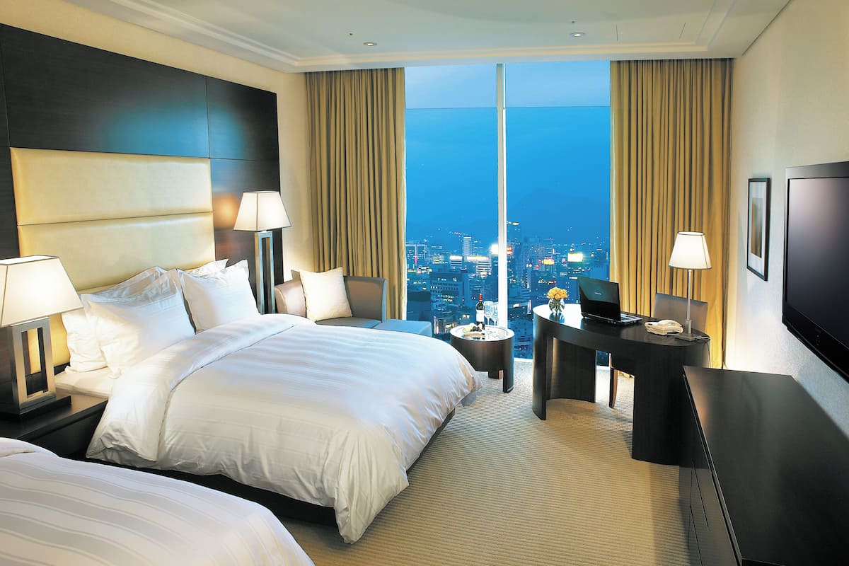 A hotel room with a large bed, a desk, a TV, and a view of the cityscape.