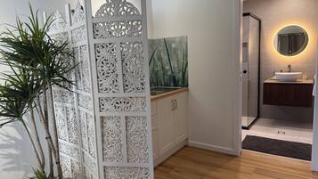 Une salle de bain moderne avec un plancher en bois, un séparateur décoratif blanc et un miroir rond avec un éclairage intégré.
