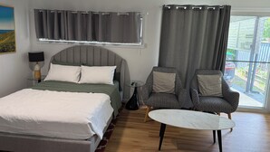 Une chambre à coucher comprenant un lit, deux fauteuils, une petite table, un ventilateur de plafond et une fenêtre avec des rideaux.