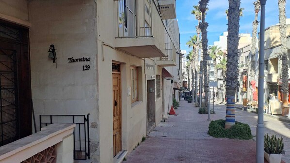 A narrow street lined with buildings, palm trees, and a pedestrian walkway.