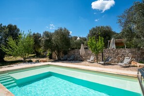 Ein rechteckiger Pool mit Stufen, umgeben von einer Steinmauer und Bäumen.