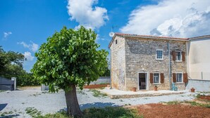 Un edificio in pietra con tetto a tegole, un albero di fronte e un cielo sereno.