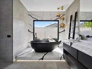 Ein modernes Badezimmer mit einer freistehenden Badewanne, Marmorböden und einem großen Fenster mit Blick nach außen.