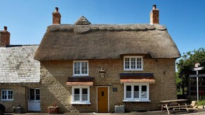 A traditional thatched-roof building with a brick facade, a wooden door, and a bench outside. - The Sun Inn (Bedford)