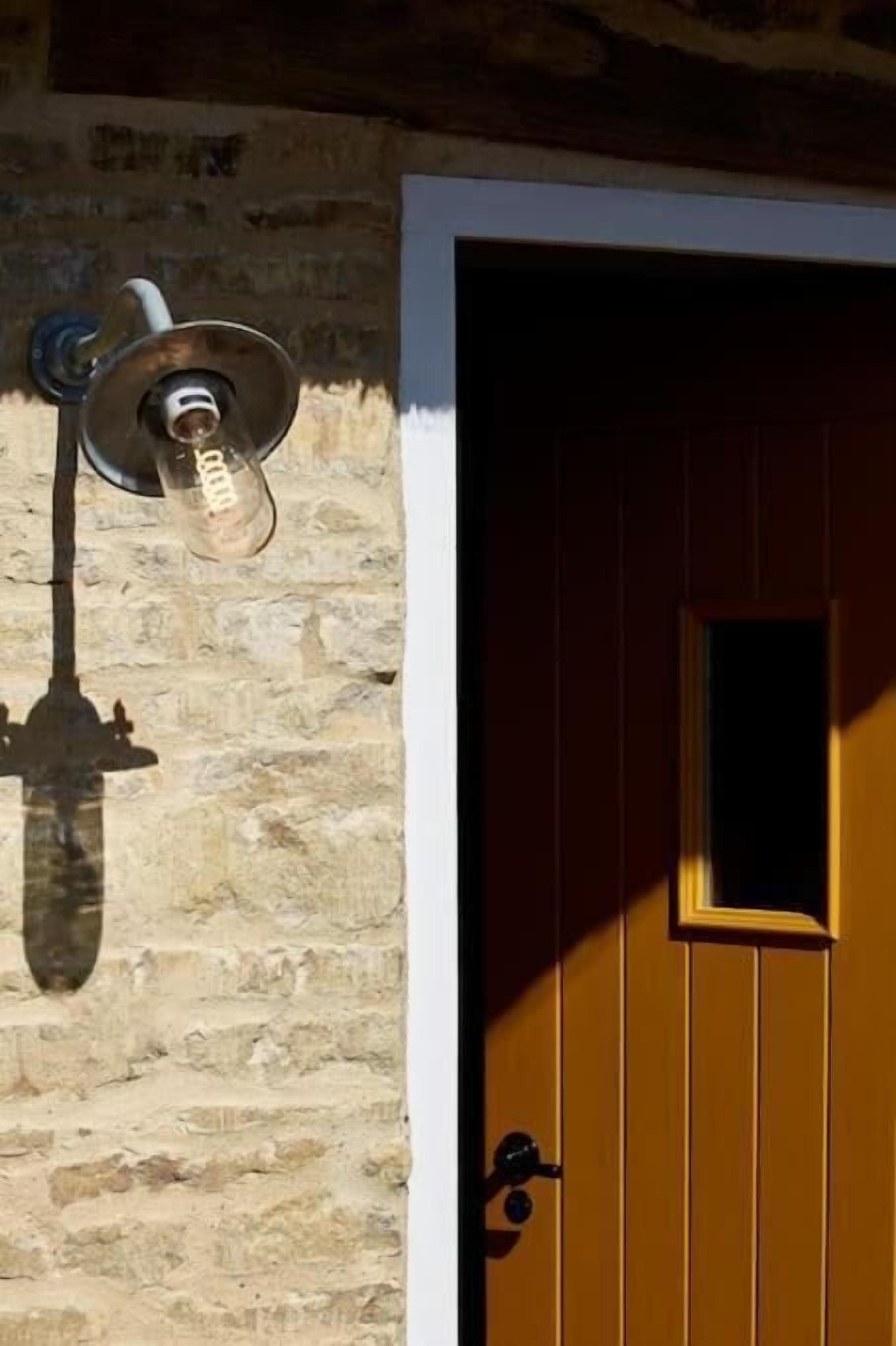 Eine rustikale Steinmauer mit einer altmodischen Leuchte und einer Holztür mit kleinem Fenster.