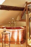 A spacious room with a large copper bathtub, wooden beams on the ceiling, and a wooden staircase.