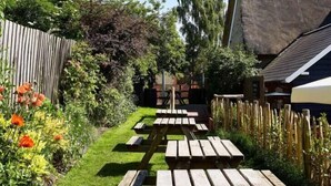 A garden with a wooden pathway leading to a picnic table area. - The Sun Inn (Bedford)