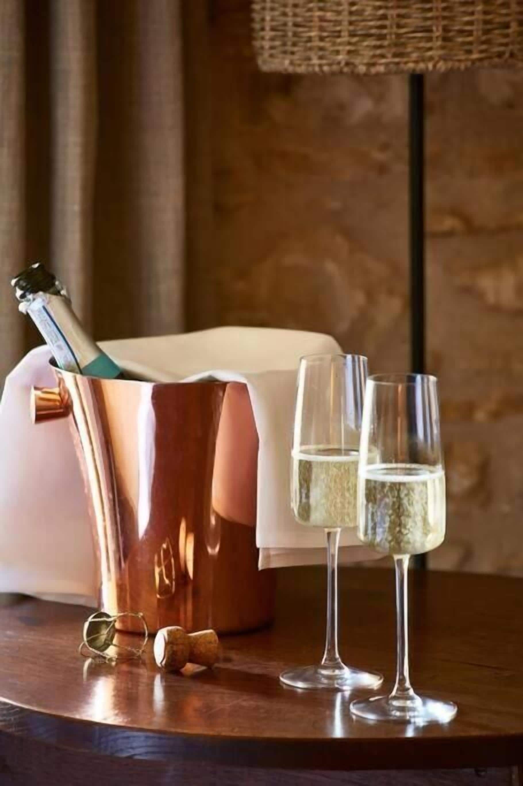 A copper champagne bucket with a bottle and two glasses on a wooden table.