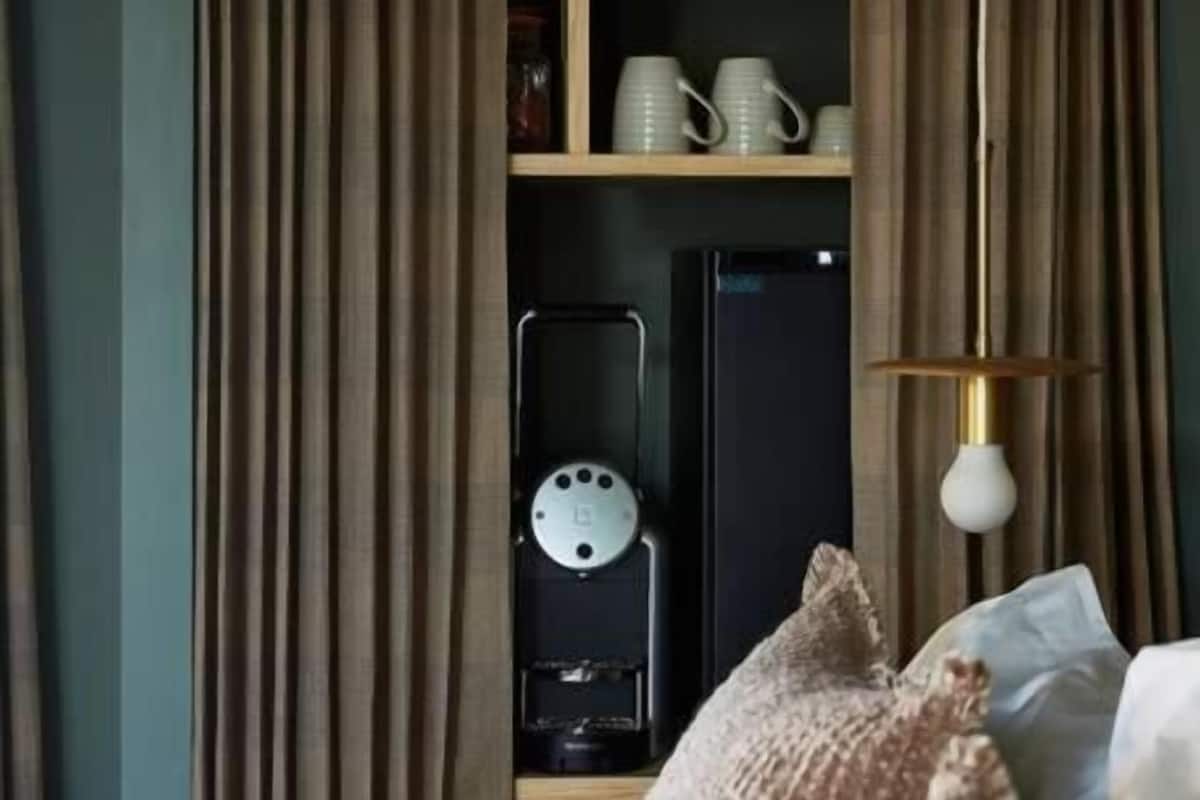 Un dormitorio con una cama, una estantería con frascos y tazas, un reloj y cortinas.