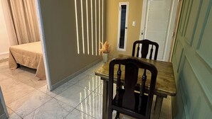 Un coin repas avec une table et des chaises en bois, un lit en arrière-plan et une porte avec une fenêtre.