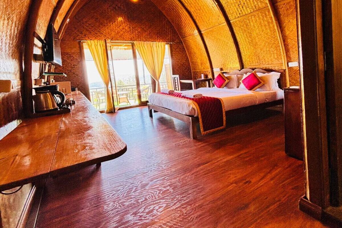 Une pièce confortable à la voûte impressionnante, dotée d’un plancher en bois, d’un lit avec des oreillers, d’une petite table avec une bouilloire et d’une fenêtre agrémentée de rideaux.