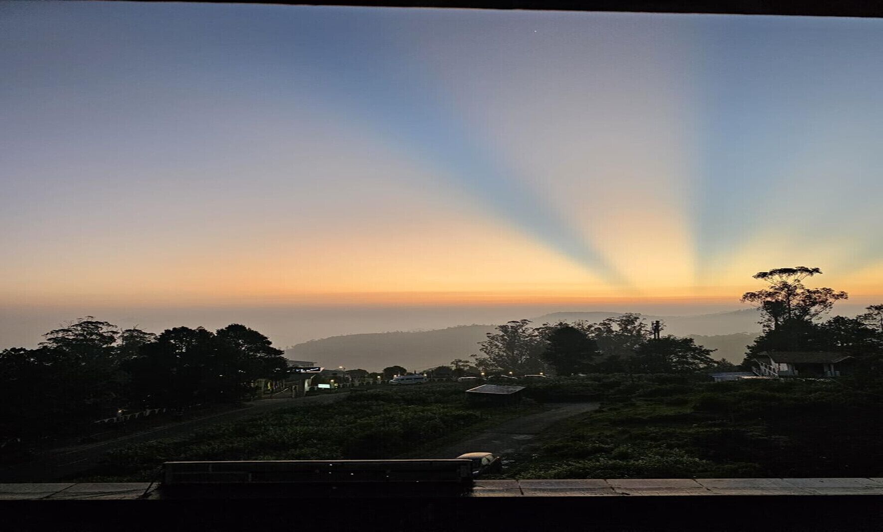 Vista al atardecer desde un punto elevado, con una carretera y árboles en primer plano.