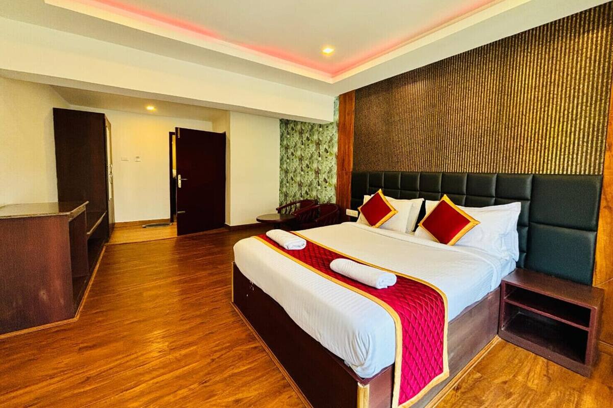 Une chambre d’hôtel avec un grand lit, un plancher en bois, une tête de lit sombre et une petite table de chevet.