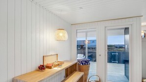 A room with a wooden bench, a small table with a basket of fruit, a wicker basket, and a large sliding glass door leading to an outdoor deck. - "Alvia" - 250m from the sea by Interhome (Løkken)