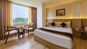 A hotel room with a large bed, two chairs, a small table with fruit, and a view of greenery through the window. - OPO Horizon Anant Ayodhya (Faizabad)