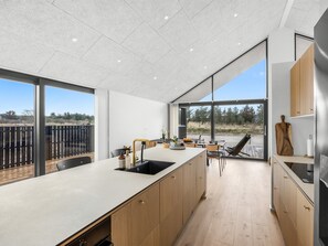 Eine moderne Küche mit einer großen Kochinsel, Holzschränken und Blick ins Freie.