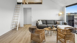 Ett modernt vardagsrum med en grå soffa, två fåtöljer i rotting, ett litet runt bord och en trappa som leder upp till en övre våning.
