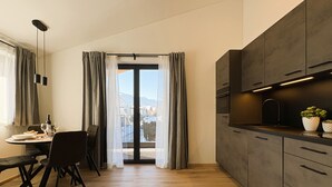Une cuisine moderne avec des meubles de couleur sombre, un coin repas avec une table et des chaises, et une vue sur l’extérieur grâce à une porte vitrée.