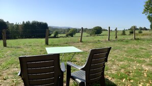 Een tafel en twee stoelen buiten, met uitzicht op een omheind veld en bomen.