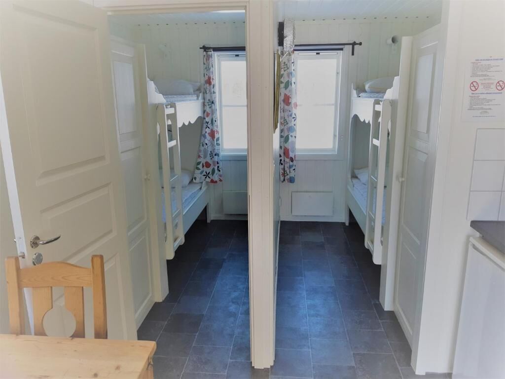 A narrow hallway with bunk beds and a wooden chair, leading to a room with a window and a door.