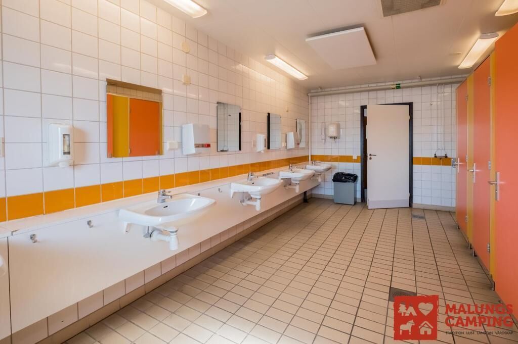 A long, white-tiled bathroom with multiple sinks and a mirror.
