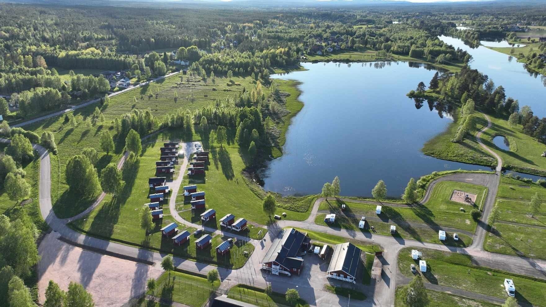 An aerial view of a campground with RVs parked in rows, a lake, and surrounding greenery.