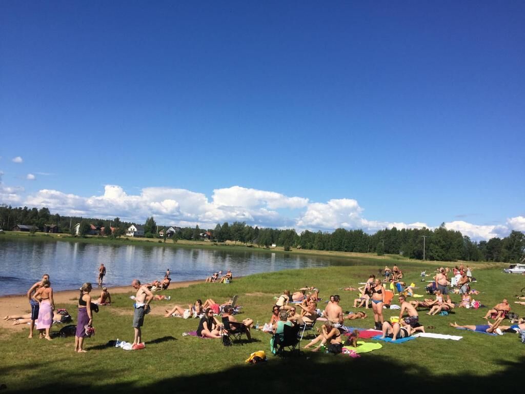 Un encuentro junto al lago, con gente descansando sobre el césped y junto al agua.