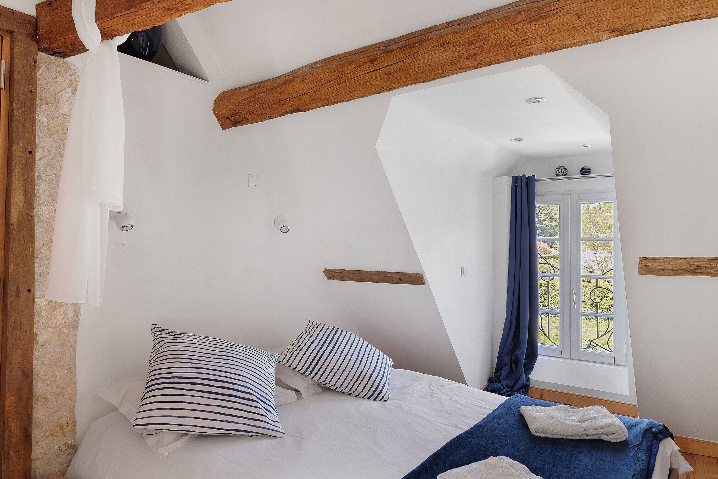 A bedroom with a sloped ceiling, a window with curtains, and a bed with striped pillows.