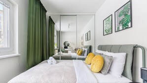A neatly made bed with a white comforter and pillows, a green curtain, and a mirror reflecting the room. - Lumina cozy 3-room apart near the metro (Warsaw)