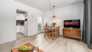 A modern living room with a dining area, a kitchen in the background, and a TV displaying "NETFLIX". - Lumina cozy 3-room apart near the metro (Warsaw)
