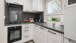 A modern kitchen with white cabinets, a black stove, and a window with a view of greenery. - Lumina cozy 3-room apart near the metro (Warsaw)