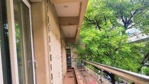A narrow balcony with a glass railing, large windows, and a view of a street with cars and trees. - Aaron Harikanta  Stayz (New Delhi)