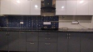 A kitchen with dark grey cabinets, a black stove, and white upper cabinets. - Aaron Harikanta  Stayz (New Delhi)