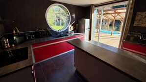 A modern kitchen with a large window, a built-in oven, and a refrigerator. - L'écrin de la forêt (Jeanménil)