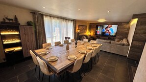 A modern dining area with a wooden table set for six, a sofa, and a TV in the background. - L'écrin de la forêt (Jeanménil)
