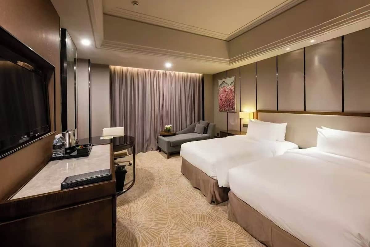 Une chambre d’hôtel avec un grand lit, un canapé, un bureau avec une télévision et une grande fenêtre avec des rideaux.