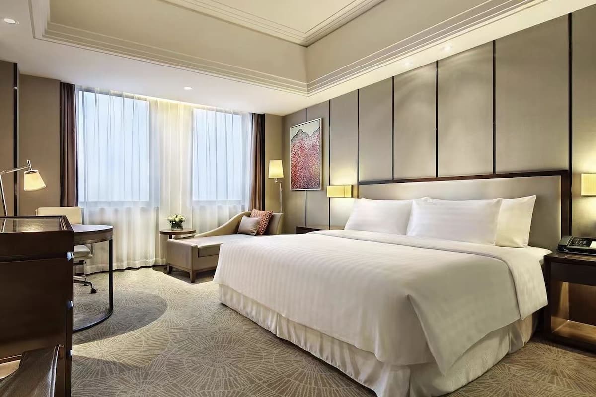 Une chambre d’hôtel avec un grand lit, un bureau, une chaise et une fenêtre avec des rideaux.