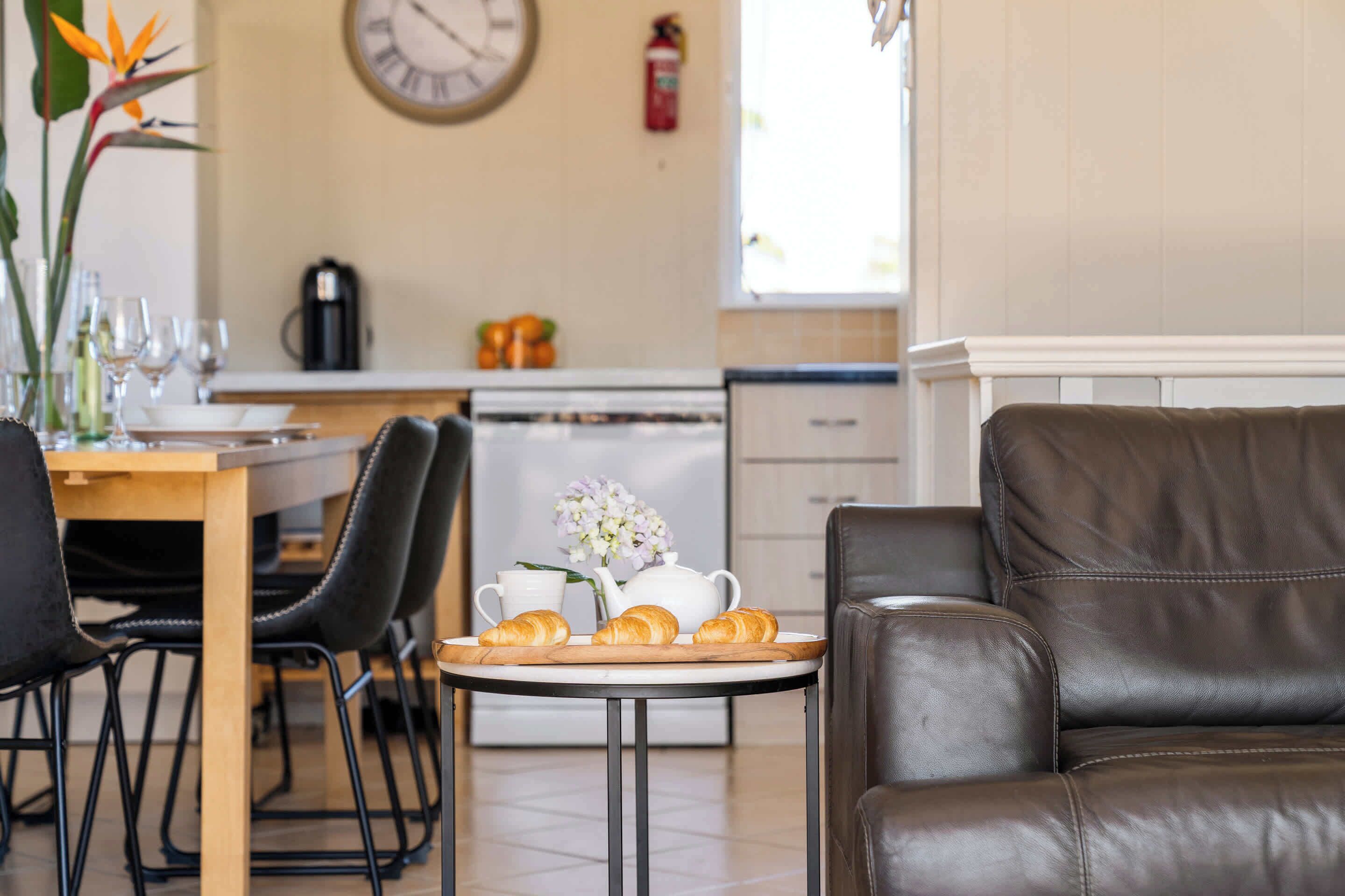 Un comedor con una mesa dispuesta para el desayuno, un sofá y una cocina al fondo.