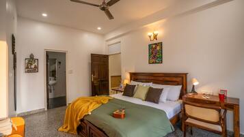 A bedroom with a bed, a desk, a chair, a ceiling fan, a wall-mounted light fixture, and a door leading to a bathroom.