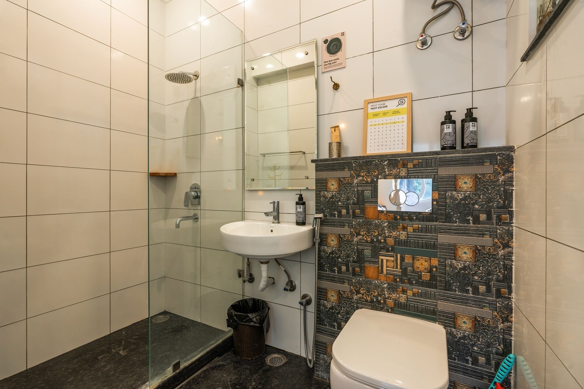 A bathroom with a glass shower enclosure, a white sink, and a toilet. There are two bottles of shampoo and conditioner on the sink.