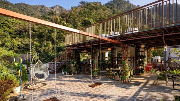 A rustic outdoor patio with a swing, seating area, and a covered structure with stairs. - LiveAway Rishikesh Laxman Jhula by PACK (Rishikesh)